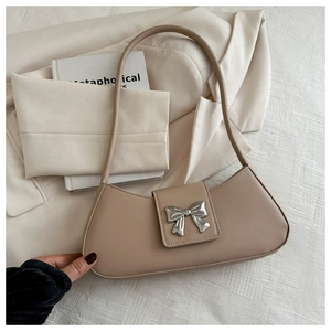 Détail du sac baguette beige clair avec nœud en métal argenté sur tissu blanc texturé