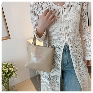 Vue détaillée du sac beige texturé avec inscription rose et bandoulière en chaîne dorée