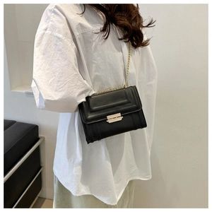 Chic black crossbody bag with geometric design and gold chain worn by a model