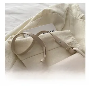Detail of a beige leather shoulder bag featuring a silver metal bow buckle and smooth strap