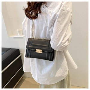 Detail of minimalist black crossbody bag with gold metal clasp on white shirt model