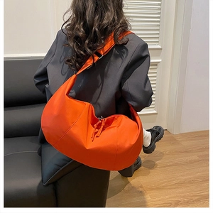 Rear view of model wearing a large orange nylon crossbody dumpling bag with adjustable strap