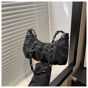 Detailed view of black pleated cloud bag with woven strap in soft indoor lighting