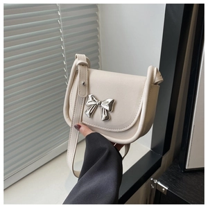 Close-up of cream white saddle bag showing the silver metallic bow buckle and leather texture
