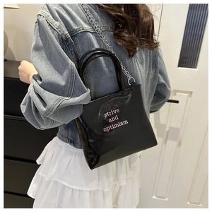 Détail du sac à main noir brillant avec typographie rose et bandoulière chaîne