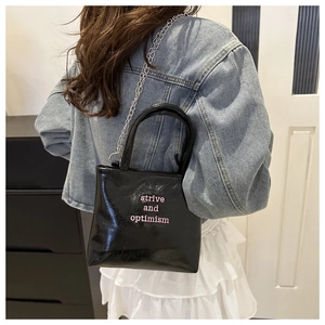 Détail du sac noir brillant avec broderie rose et fine bandoulière en chaîne argentée