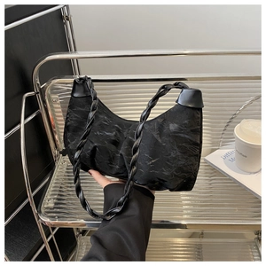 Close-up of black crinkled nylon shoulder bag with a woven handle in a modern cafe setting