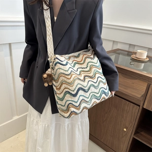 Detail of colorful striped velvet tote bag featuring a woven strap and plush pompom accessory