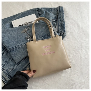 Détail de la broderie rose sur le petit sac seau en similicuir beige avec chaîne argentée