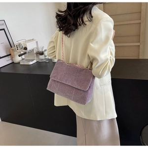 Detail view of purple glitter chain shoulder bag worn over a beige suit jacket