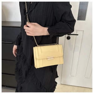 Detail view of cream chain square bag with gold buckle on black dress model