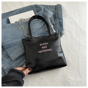 Gros plan du sac en cuir verni noir avec broderie rose strive and optimism détaillée