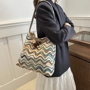 Detail of colorful woven tote bag with wave stripes and plush monster charm on shoulder