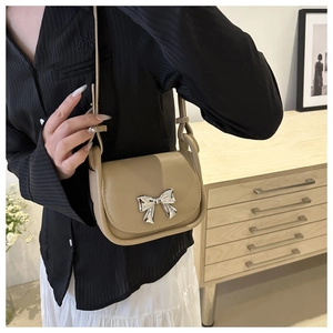 Detail view of a khaki saddle bag featuring a silver metal bow buckle on a leather flap