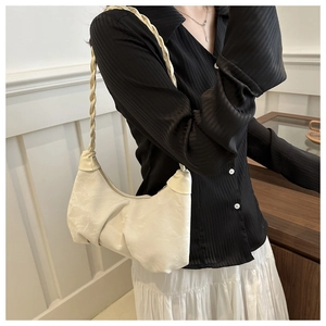 Detail of a creamy white pleated cloud bag with a braided shoulder strap on a model