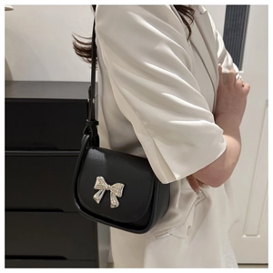 Detailed side view of black saddle bag featuring a polished silver metal bow buckle