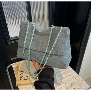 Detail of silver glitter chain tote bag featuring gold and light blue woven strap