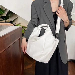 Close-up of white oversized tote bag with adjustable strap worn on woman in grey suit