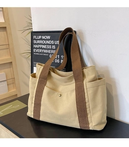 Detail of canvas tote bag with brown straps, large front pocket and metal snap button
