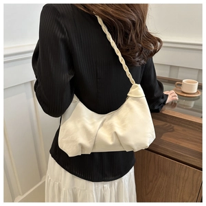 Detail of white pleated crescent bag featuring an intricate braided shoulder strap design