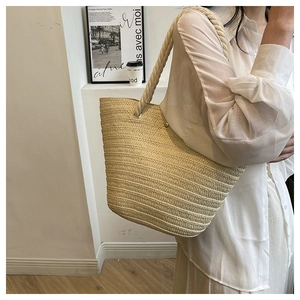Detailed close-up of the woven texture and rope handles on the beige straw tote bag