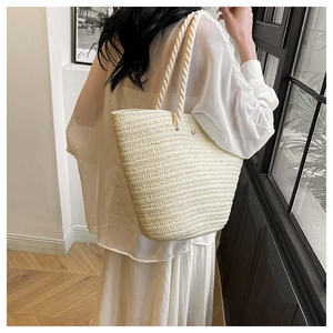 Detail of a large off-white woven tote bag with thick rope handles shown on a model