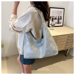 Detail of soft metallic silver hobo tote bag with brand logo shown in a home setting