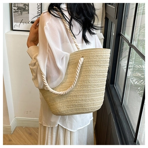 Detail of beige straw tote bag with white rope handles worn by model in minimalist room