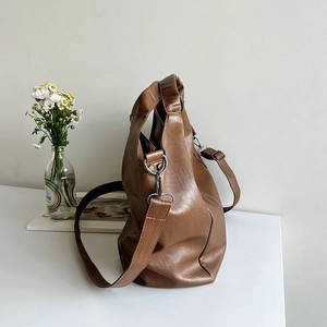Detailed view of brown PU leather tote bag with silver hardware on a minimalist white desk