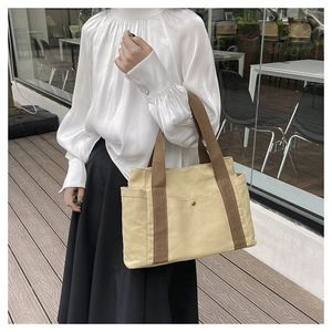 Detail of canvas tote bag with brown straps and side pocket in an urban setting