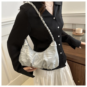 Detail of silver pleated crescent bag showing metallic texture and woven shoulder strap