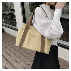 Detail of canvas tote bag with front snap pocket and side compartment worn by model