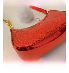 Detail of red faux-crocodile texture on crescent bag with gold chain and plush charm