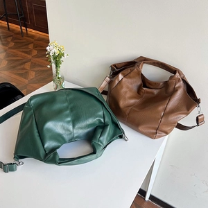 Detail view of slouchy PU leather tote bags in dark green and caramel brown with straps