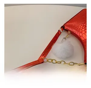 Detail of red croc-effect crescent bag with gold chain strap and white pompom charm