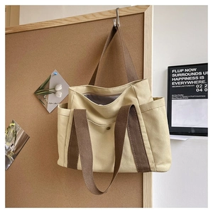 Detail of canvas tote bag showing brown handles, side pocket, and metal snap closure