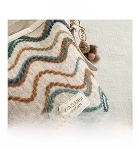 Close-up of striped knit bag with leather brand tag, gold metal ring and plush pompom charm