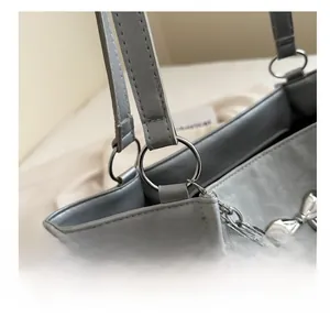 Détail de la breloque papillon argentée et chaîne sur un sac à main gris soyeux