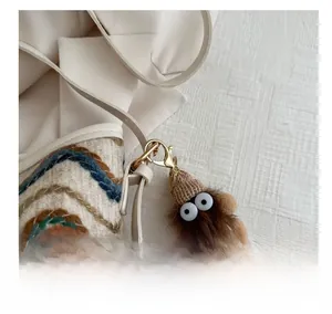Close-up of a cute brown plush charm with a knitted hat on a beige leather bag strap