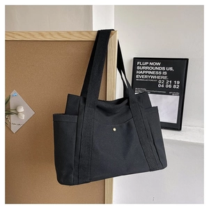 Close-up of black canvas tote bag showing side pocket, gold snap button, and woven strap