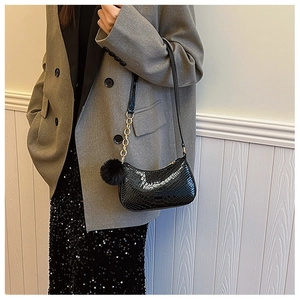 Detail of black faux leather shoulder bag with crocodile texture and gold chain on model