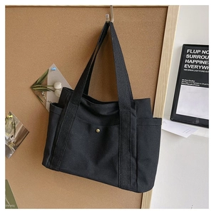 Detail view of the black canvas tote bag showing the front snap pocket and side storage