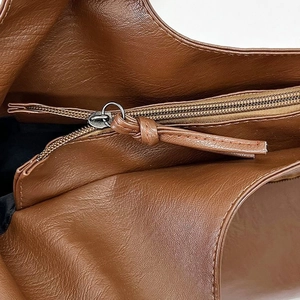 Macro detail of the smooth metal zipper and brown leather pull on the shoulder bag