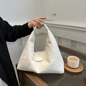 Minimalist cream white hobo bag in soft matte texture held by a model in a cafe setting