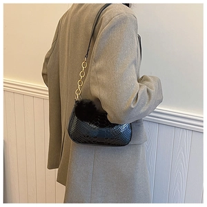 Detail of black faux snake skin shoulder bag with gold chain and plush charm accent