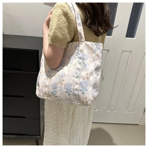 Dettaglio della borsa tote color crema con motivi di ortensia indossata a spalla