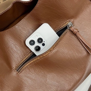 Detail of dark brown leather bag showing spacious back zipper pocket with smartphone