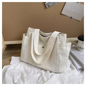 Detail view of white canvas tote bag with side pockets and metal buckle on cork background