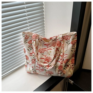 Dettaglio di una borsa tote in tela crema con vivaci motivi floreali rossi e tasca esterna
