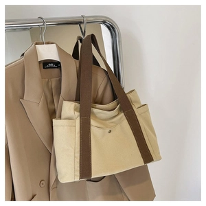 Detailed close-up of a cream canvas tote bag with brown straps and side pockets
